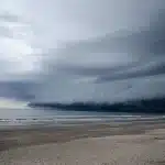 Palmen biegen sich im starken Wind, während Regenschauer und Wellen die Küste treffen