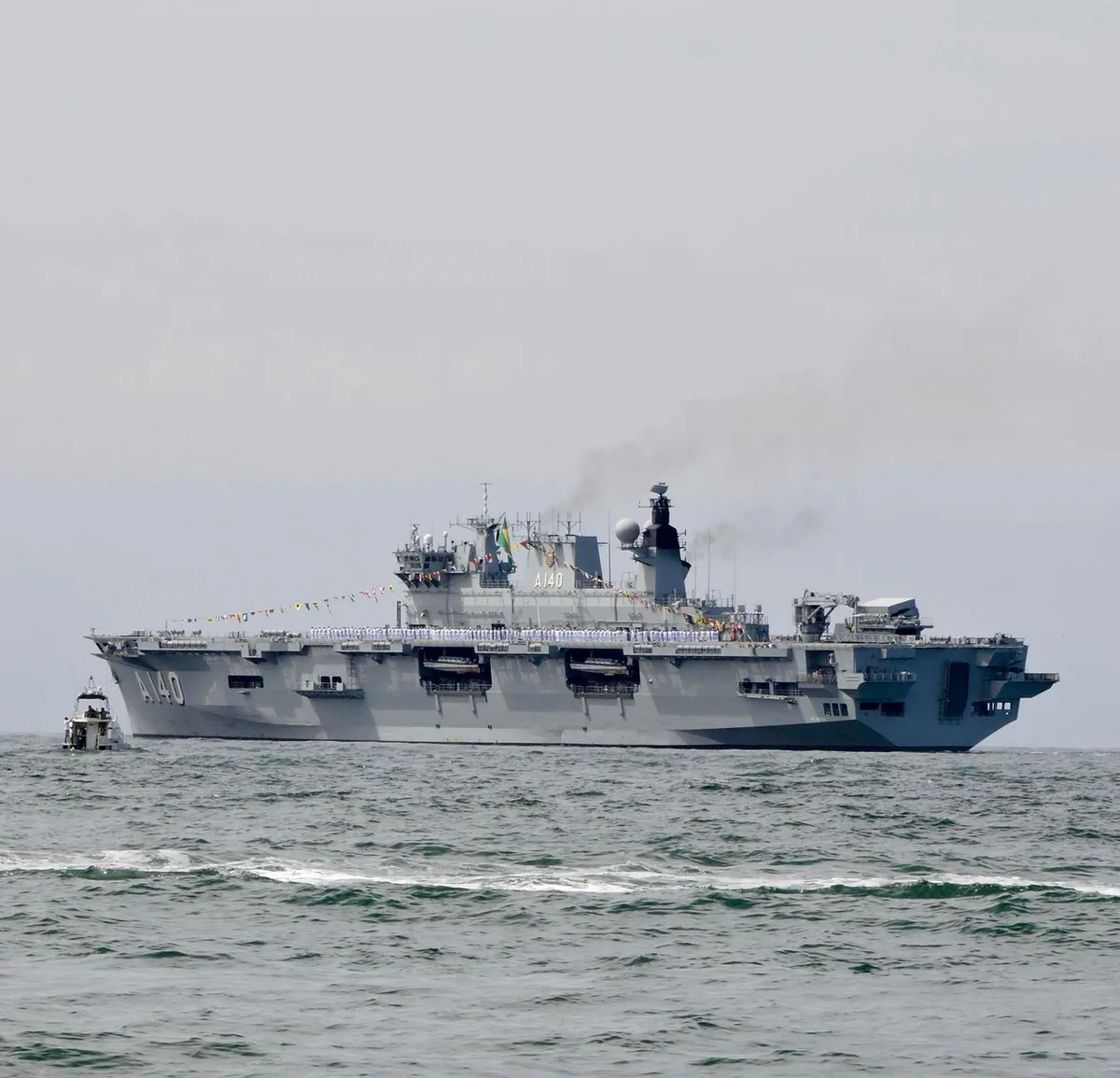 Aircraft carrier approaching a tropical port with sailors visible on deck