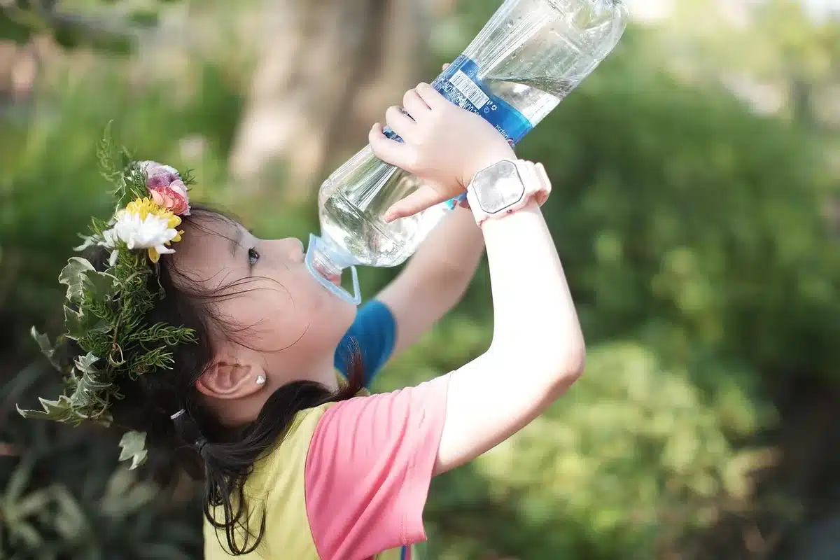 Kind trinkt Wasser während einer Schulaktivität im Freien an einem heißen Tag.