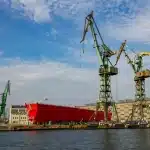 silhouette of a large warship hull at a shipyard pier under clear daylight